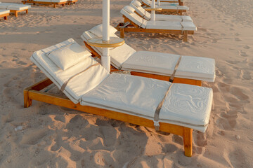 Close-up of soft white sun loungers on a sandy beach in the morning being cleaned by staff