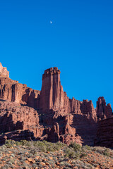 Fototapeta premium Moon rising over Fisher Towers off Scenic Byway 128 near Moab, Utah on clear winter afternoon.