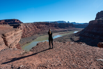 Woman photographs Colorado River from overlook on Potash Road near Moab, Utah on clear sunny winter day.