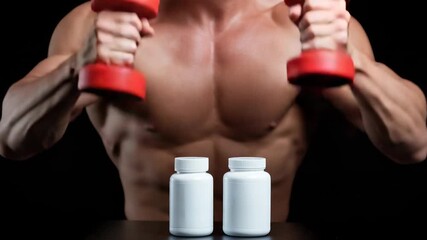 Energetic bodybuilder lifting dumbbells with supplement bottles in focused gym workout