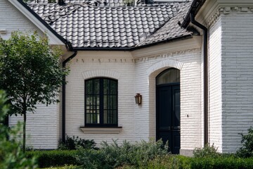 Beautiful white house with black roof and green bushes during daytime in a residential area surrounded by trees and plants