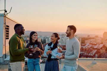 Group of diverse friends enjoying a social gathering on a city rooftop, drinking wine, laughing,...