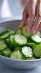 Hand gently tapping container to settle cucumber slices in bowl, concept of Shakeable cucumber salads  