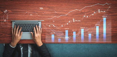 A businessman works on a laptop analyzing financial data with ascending charts and graphs on a wooden table, illustrating investment strategies and market insights. Scalp