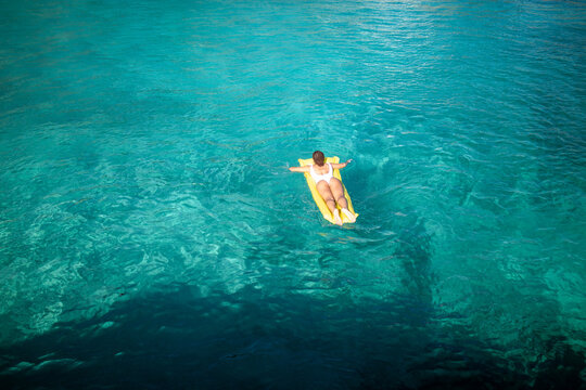 Person relaxing on inflatable mattress in clear turquoise sea