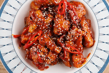 Delicious sweet and spicy chicken served in a bowl with chili and sesame toppings for a flavorful...