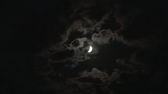 A Waxing Moon and flying clouds in the moonlight against a dark sky. A spooky cloudy night, like thriller and horror films. Real video recording