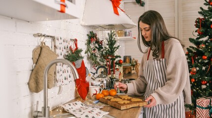 Young woman baking Christmas cookies in a festive kitchen decorated with a tree and lights