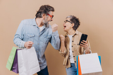Plakat Cheering senior couple celebrating success grabbing shopping bags