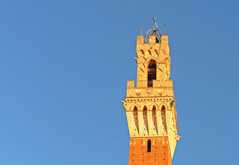 Naklejka premium Famous bell tower 'Torre del Mangia' on the Piazza del Campo in the evening sun on a bright october day with blue sky in Siena, Tuscany