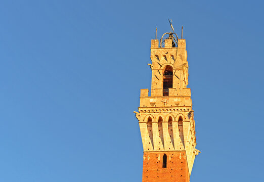 Famous bell tower 'Torre del Mangia' on the Piazza del Campo in the evening sun on a bright october day with blue sky in Siena, Tuscany