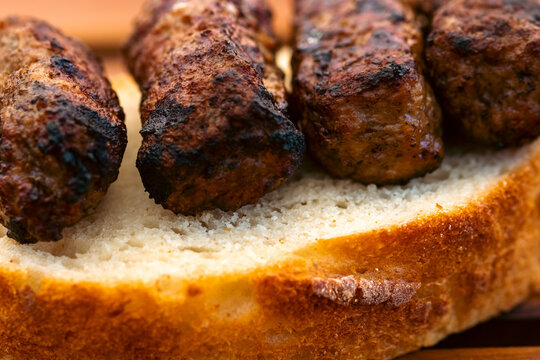 Preparing traditional Romanian meat rolls called mici or mititei on a hot barbecue grill with fire flames