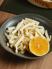 Fringed cheese with citrus slice in ceramic bowl, Shredded string cheese with orange slice in ceramic bowl on wooden table