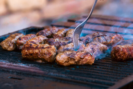 Preparing traditional Romanian meat rolls called mici or mititei on a hot barbecue grill with fire flames