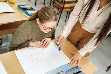The students are taking an exam in the classroom, focused on their papers. The teacher walks around the room, quietly checking on their progress.	
