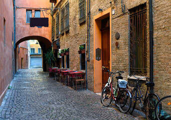 Cozy narrow street with tables of trattoria and bicycls in Ferrara, Emilia-Romagna, Italy. Ferrara is capital of the Province of Ferrara