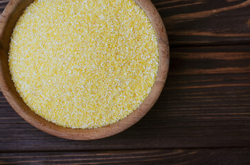 Rustic wooden bowl with yellow cornmeal on dark table