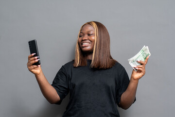 happy nigerian lady holding her phone and new naira notes