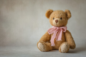 Brown Teddy Bear Sitting with Pink Bow on Beige Background