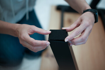 Woman assembles furniture. She is focused on attaching black adhesive felt pad for furniture legs of wooden table.