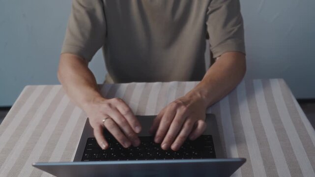 Close up from above of male hands typing on a laptop keyboard. Natural hand posture, smooth finger motion and calm everyday computer activity indoors. High quality 4k footage