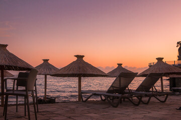 Pink sunset on the Adriatic Sea. Beach with umbrellas and sun loungers