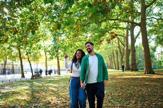 Cheerful diverse couple walking in London park, holding hands admiring the view. Image with copy space.