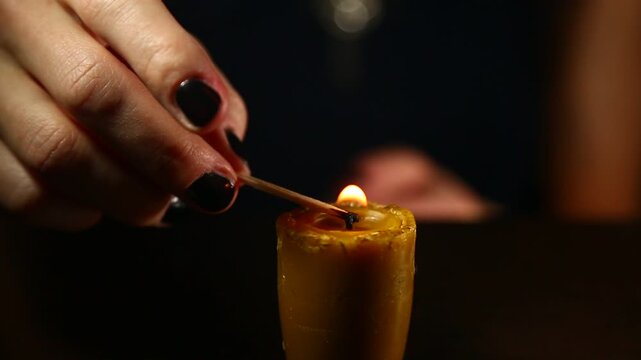 Woman hand lights a match the bees wax candle for mood, relaxation, meditation dark black background. Person lighting the decoration handmade single candle flame. Closeup