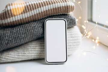 Smartphone mockup on cozy sweaters with festive bokeh lights.