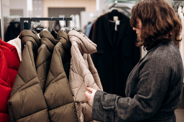 Stylish young woman selecting a winter jacket in a modern clothing store.