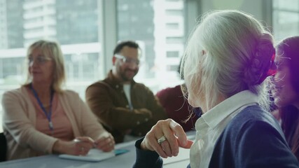 A cheerful senior woman actively participates in a professional meeting, smiling and pointing. She engages with colleagues, fostering collaboration and communication.