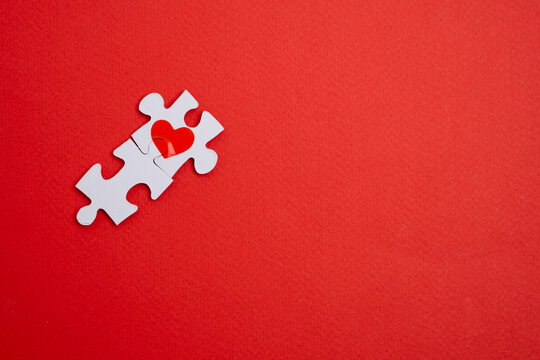 Two joined puzzle pieces with red heart on red background. Perfect Match.