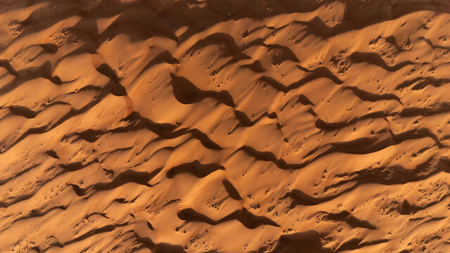 Aerial view of rolling sand dunes with shadows creating a textured landscape under the desert sun, Bidiyah, Ash Sharqiyah North Governorate, Oman.