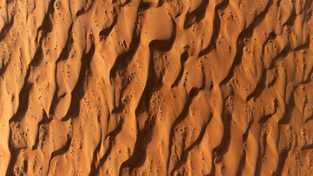 Aerial view of the undulating, sun-kissed sands create mesmerizing patterns and shadows across the vast desert landscape, Bidiyah, Ash Sharqiyah North Governorate, Oman.