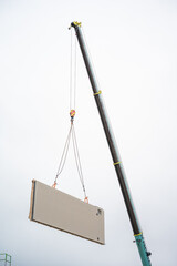 Bauteile eines Fertighauses wird mit Baukran auf Bodenplatte gesetzt. Bauteil ist vor Himmel klar zu erkennen.