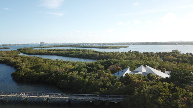 Aerial view of lush mangrove islands threaded with waterways, surrounding the white-roofed Manatee Lagoon, a vibrant contrast against the clear sky, West Palm Beach, Florida, United States.