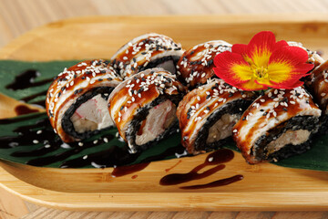 Sushi rolls with eel sauce and sesame seeds on a wooden plate with a flower garnish