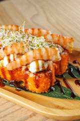 Sushi rolls topped with shrimp and sauce served on a wooden plate in a restaurant setting