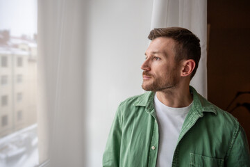 Thoughtful bearded handsome man with focused tranquil expression calmly looking at window, engaged in thinking process, brainstorming new work ideas, reflecting on life and finding inspiration.