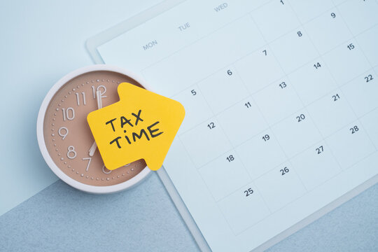 Tax time concept. Reminder sticker on clock and calendar background
