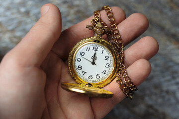 A person holds a classic gold pocket watch in their hand. The watch has a white face with black numbers.  
