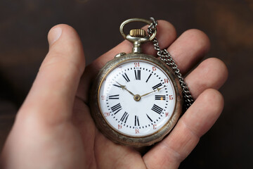 A man holds a vintage pocket watch with a white clock face and black numbers. Vintage pocket watch in classic style with chain.