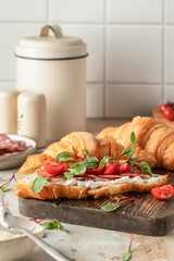 Croissant sandwich with salami, sausage, cherry tomatoes, soft cheese and chard micro greens on wooden board kitchen table background for savory healthy breakfast