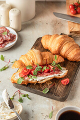 Croissant sandwich with salami, sausage, cherry tomatoes, soft cheese and chard micro greens on wooden board kitchen table background close up for savory healthy breakfast