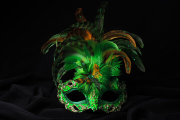 Venetian green carnival mask. A green mask with colorful feathers rests on dark fabric. 