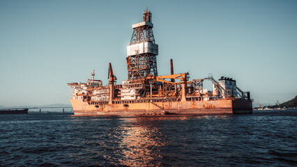 Offshore oil drilling rig ship floating on calm sea at sunset, industrial petroleum platform with derrick tower and cranes, energy production concept, wide-angle shot
