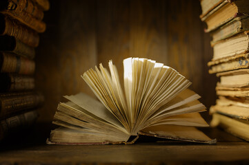 An open book rests on a wooden surface surrounded by books. The light softly illuminates its pages. The setting is a library filled with shelves of books.