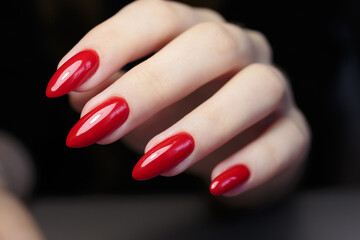 Elegant red nails showcased with a hand positioned on a dark surface in a beauty setting during a salon appointment