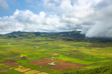 Panoramic view of the colorful agricultural fields from Serra do Cume lookout on Terceira Island, Azores, Portugal. Lush green, yellow, and brown farmlands form a scenic patchwork landscape 