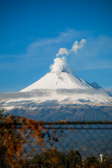 Breathtaking view of Popocatepetl volcano in Mexico, featuring a snow-capped summit emitting a large smoke plume under a clear blue sky